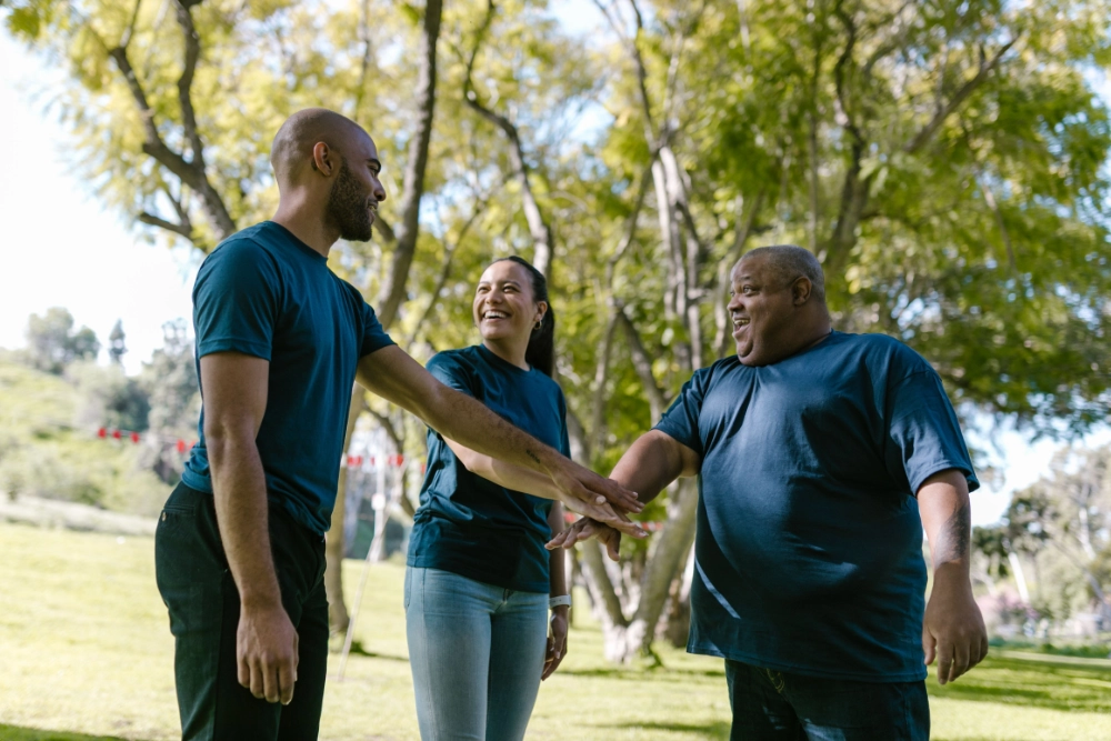 Three people in a park smiling and holding hands.